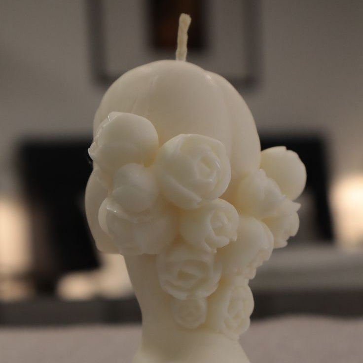 White candle shaped like a woman's torso with floral details on a textured surface.