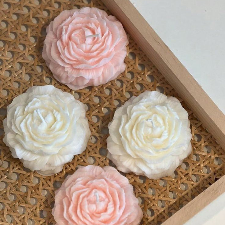 Four flower-shaped soap bars in pink and white on a woven mat