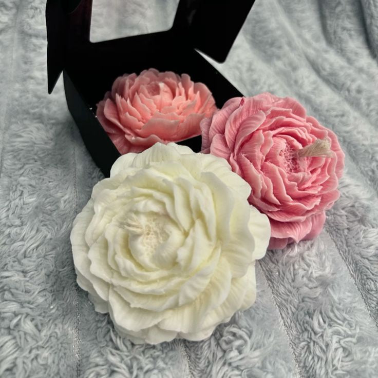 Three floral-shaped soaps in a black box on a textured gray surface