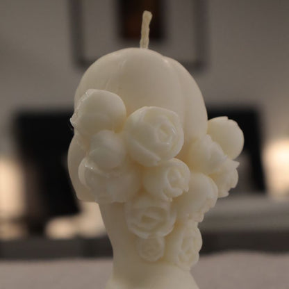 White candle shaped like a woman's torso with floral details on a textured surface.