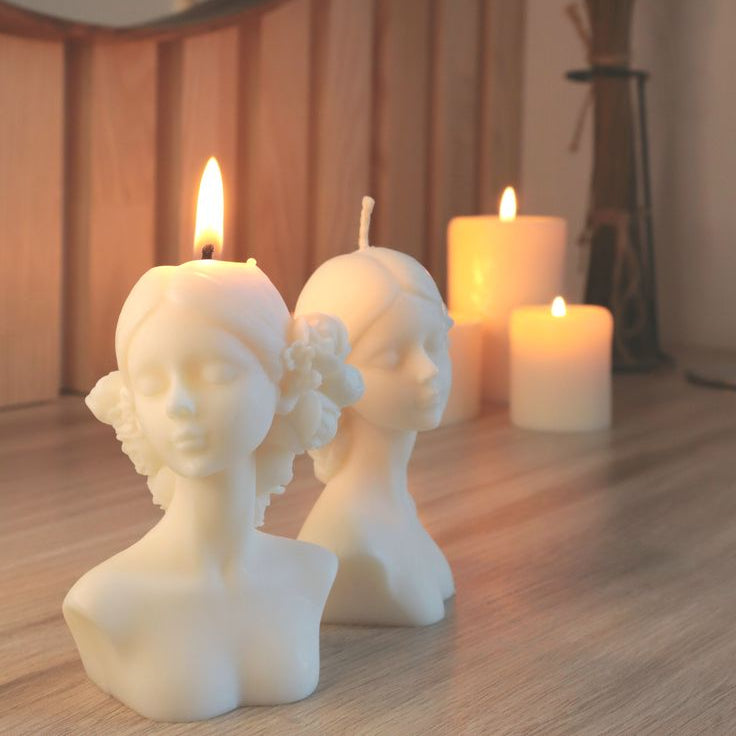 Candle holders shaped like busts with lit candles on a wooden surface.