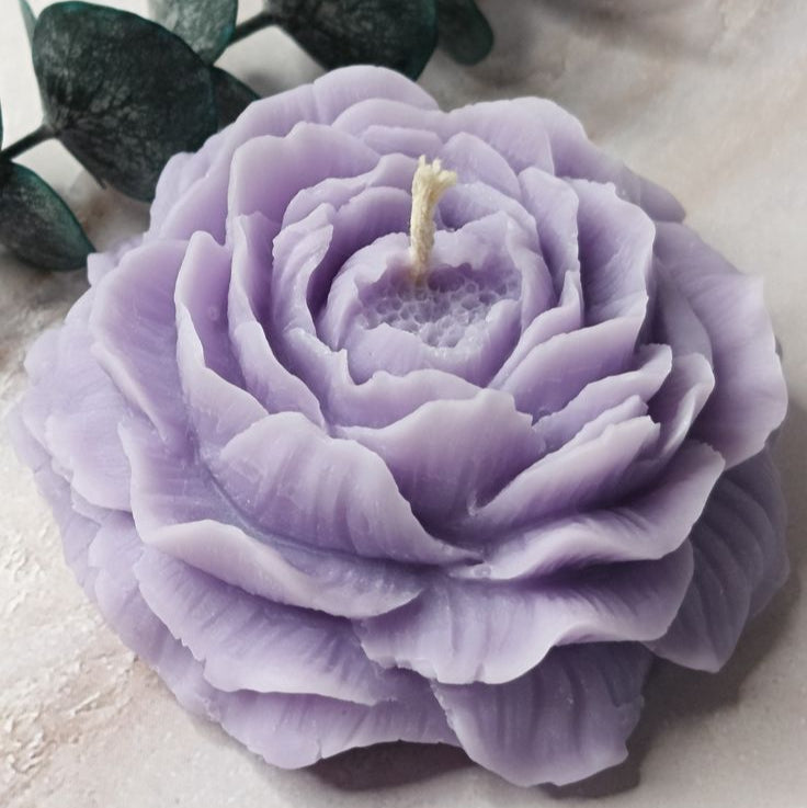 Purple flower-shaped candle with green leaves on a light background